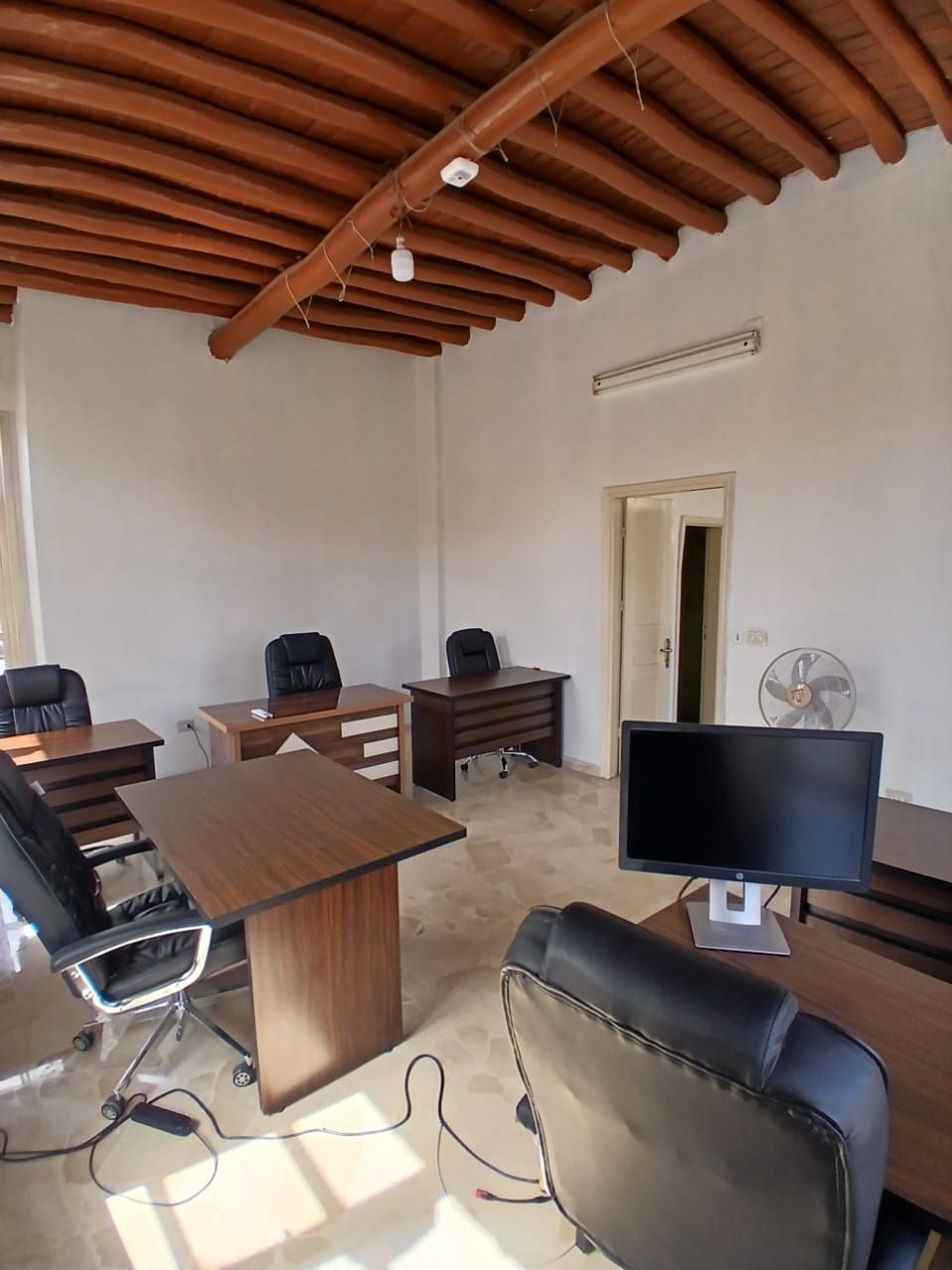 Open-plan office with several desks under a wooden-beamed ceiling